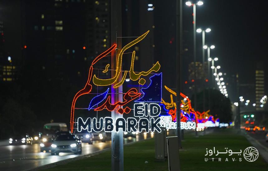 جمله «عیدکم مبارک» به فارسی و عربی نوشته‌شده با نورهای رنگی که به تیر چراغ برق آویزان شده‌است.
